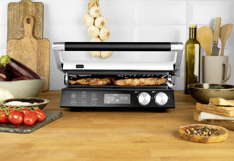 4-in-1 Multigrill auf einem Tisch mit gegrilltem Essen und frischen Zutaten.