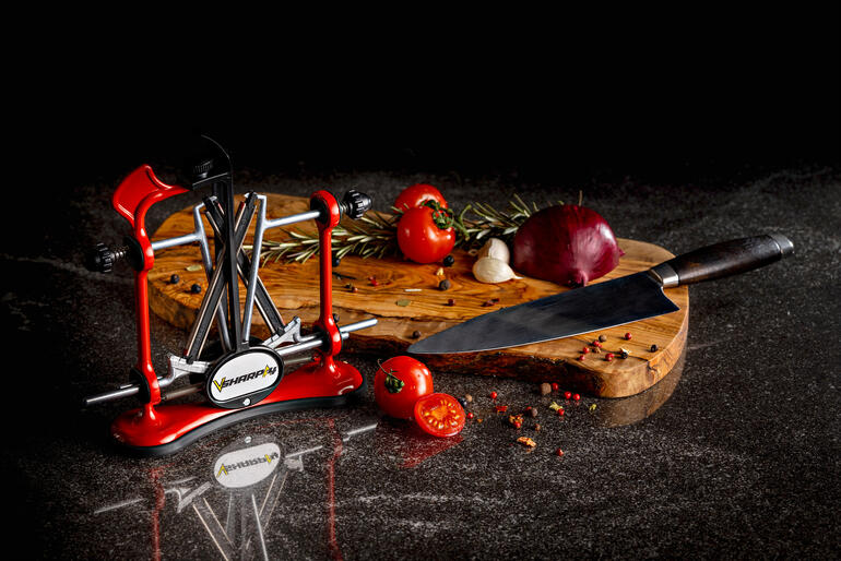 Profi-Messerschärfer in rot neben frischen Zutaten auf einem Holzbrett.