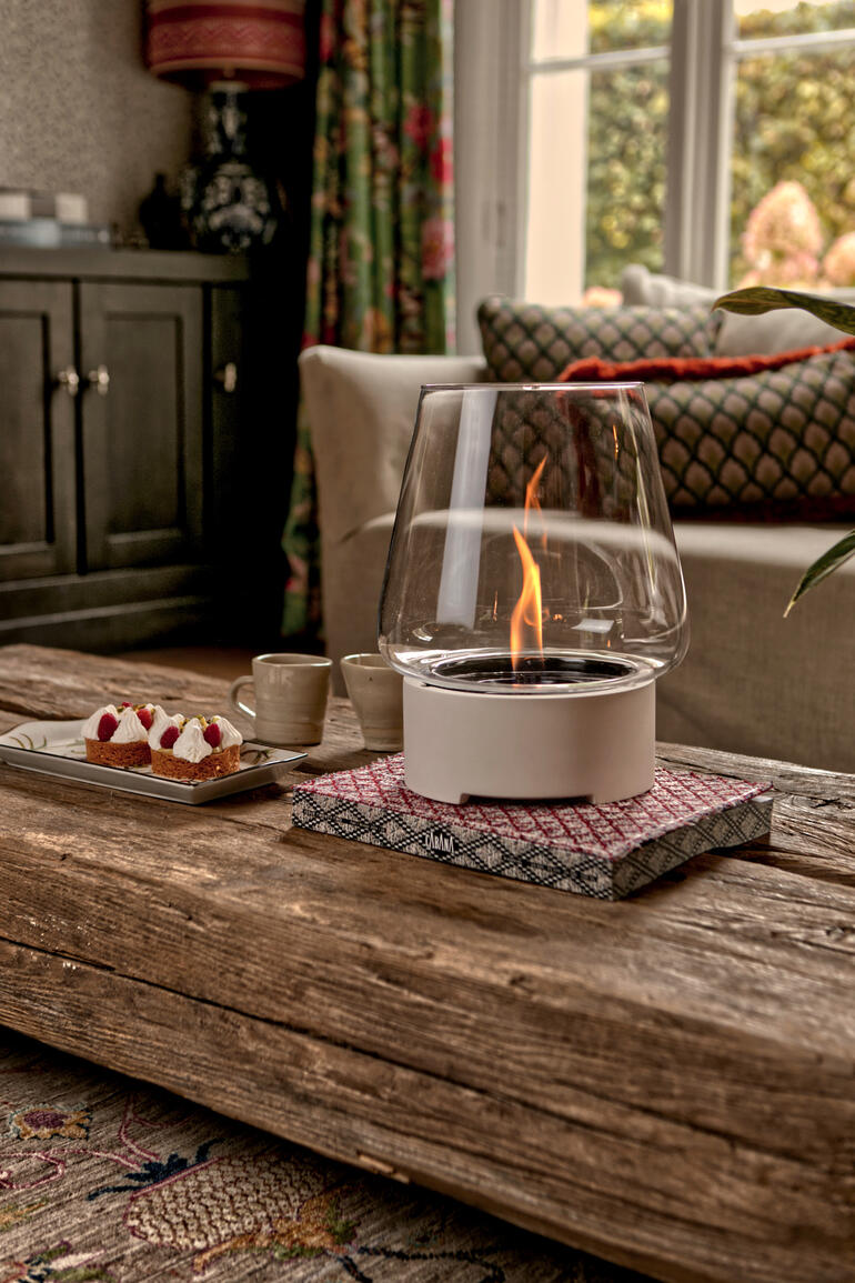 Tischfeuer in einem modernen Glasbehälter auf einem Holztisch.