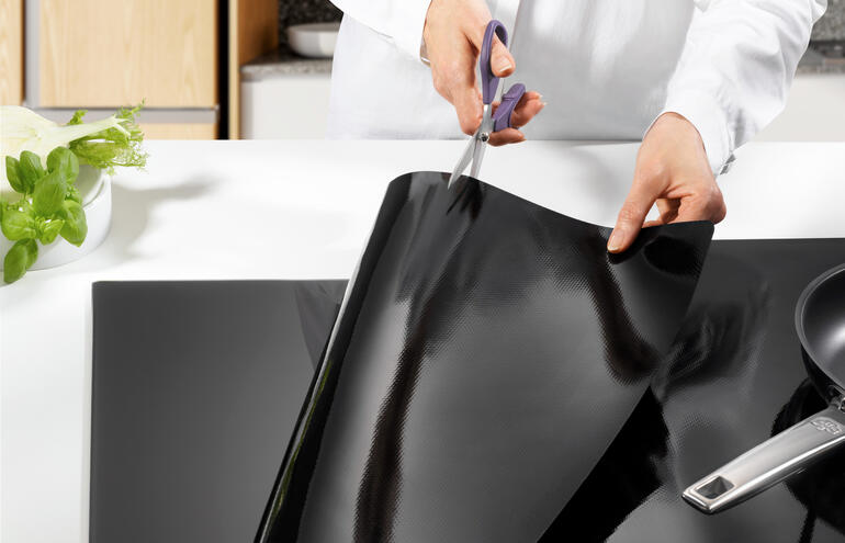 Jemand, der einen Induktions-Kochfeldschutz aus Platin zurechtschneidet