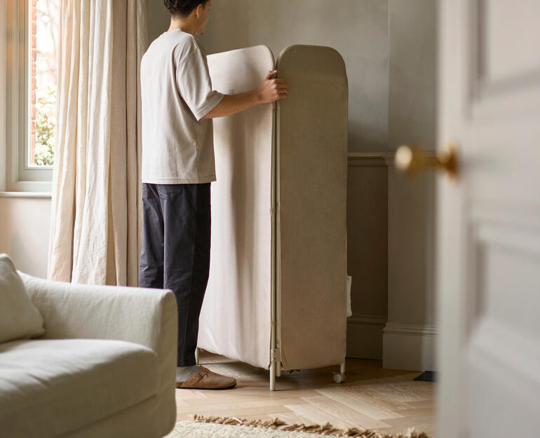 Person stellt den Wäscheständer Paravent im Raum auf.