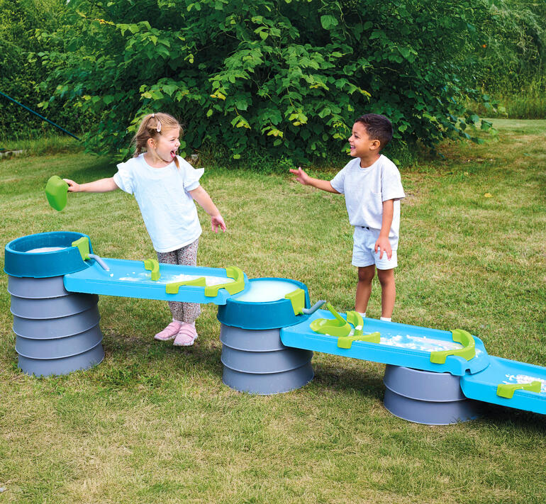 Zwei Kinder lachen und spielen an der Wasser- und Matschbahn.