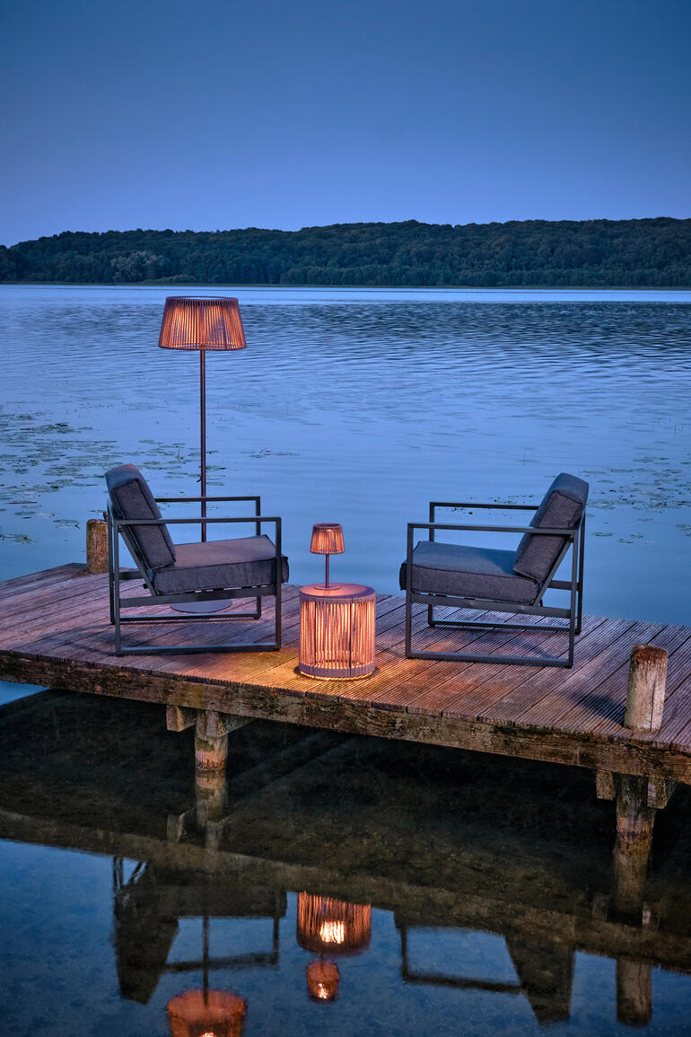 Outdoor-Tisch mit LED-Beleuchtung am Wasser, umgeben von Stühlen.