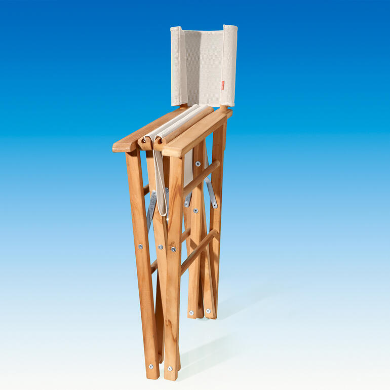 Ihr Teak-Regiesessel ist mit einem Handgriff auf schmale 17 cm zusammengeklappt und Platz sparend verstaut. Teak-Regiesessel in aufrechter Position vor einem blauen Hintergrund.