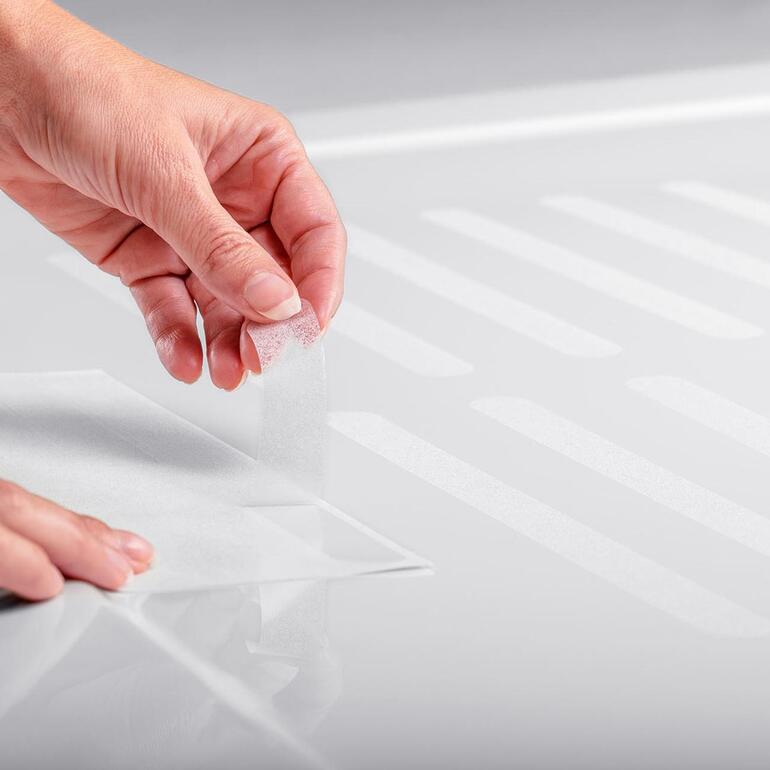 Eine Hand klebt einen Rutschschutz-Streifen auf einen Duschboden