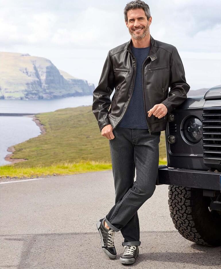 Grey-Denim-Jeans Mann in schwarzer Lederjacke vor Geländewagen in der Natur.