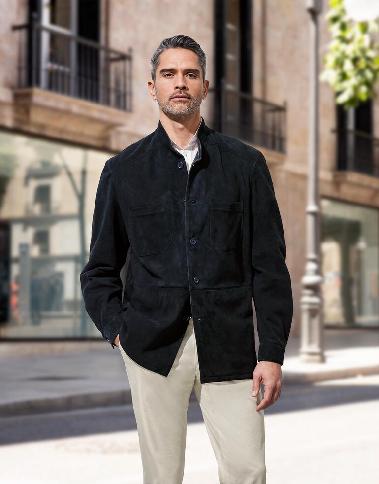 Rentierkalbleder-Hemdjacke Mann in schwarzer Rentierkalbleder-Hemdjacke, steht vor moderner Architektur in der Stadt.