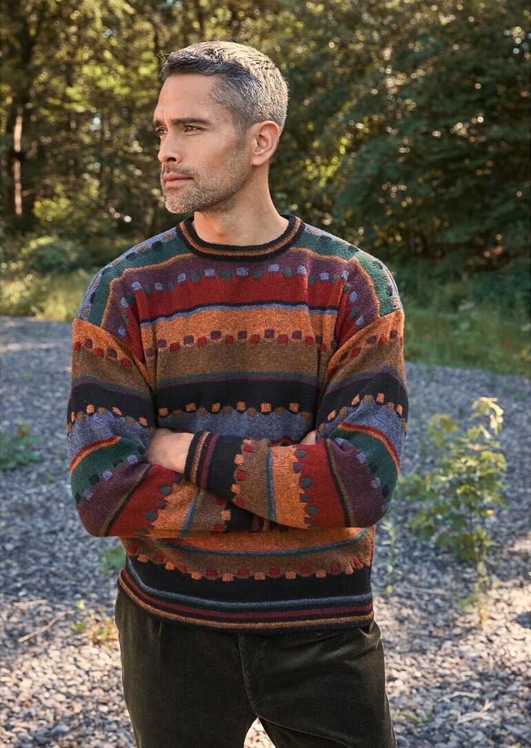 Mann in buntem Pullover steht in einer grünen Umgebung.