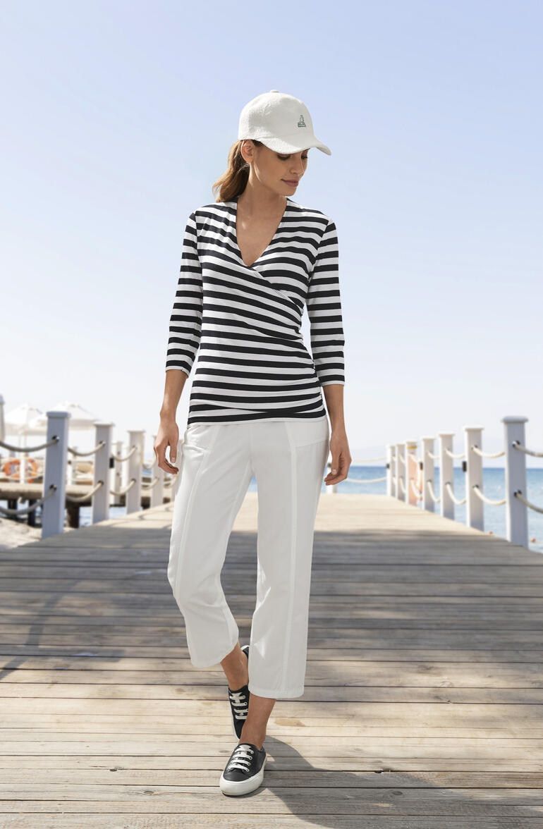 Schwarz Frau in gestreifter Bluse und weißen Hosen, am Strand.