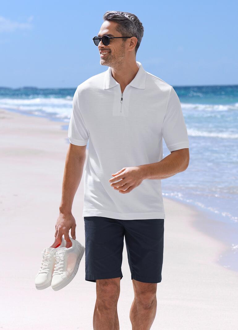 Weiß Mann in weißem Poloshirt und schwarzer Shorts am Strand.