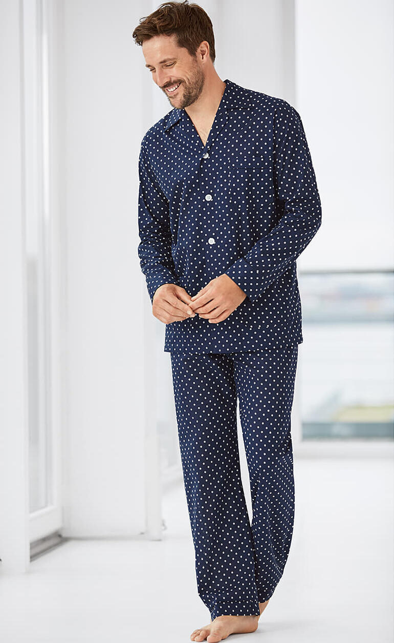 Mann in Navy-Pyjama mit weißen Punkten, lächelnd im Raum.