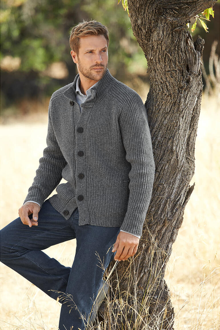 Grau Mann in grauem Fisherman Raglan Cardigan lehnt an einem Baum.