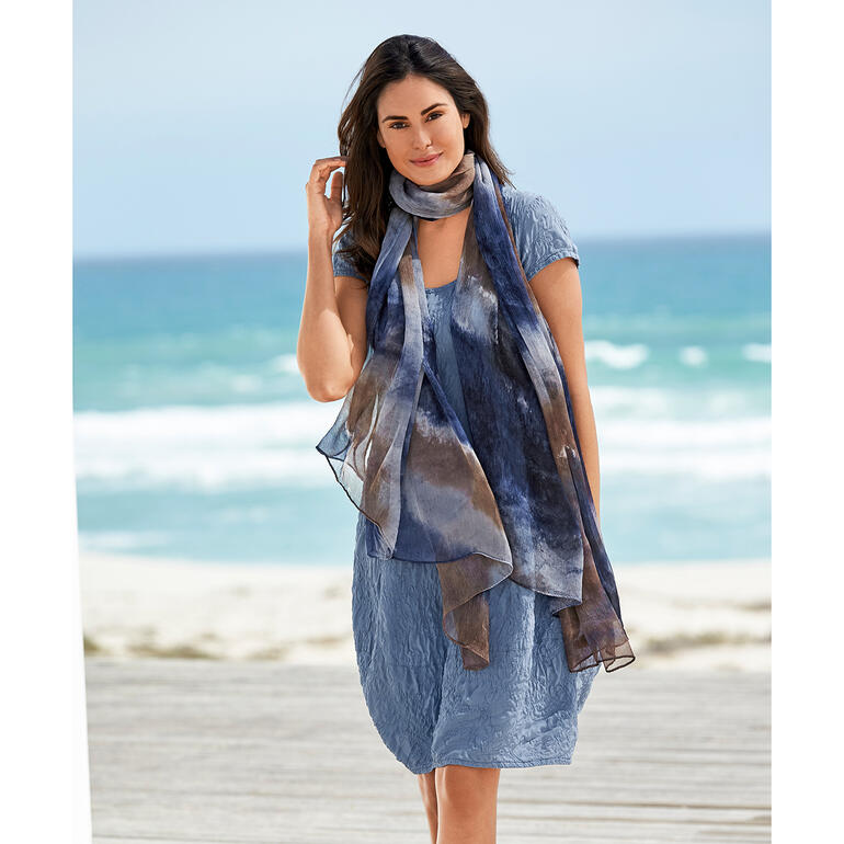 Seidencrash-Sommerkleid Frau in einem blauen Seidencrash-Sommerkleid läuft am Strand mit Schal.