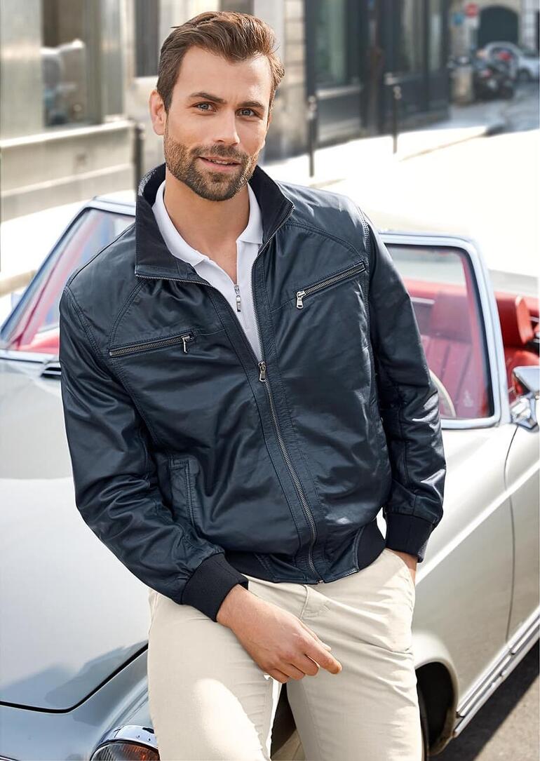 Mann posiert im blauen Sommer-Lederblouson vor einem Auto.