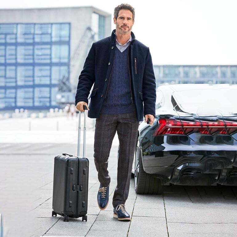 Wollwalk-Sakko Mann mit Wollwalk-Sakko am Flughafen, neben einem schwarzen Auto.