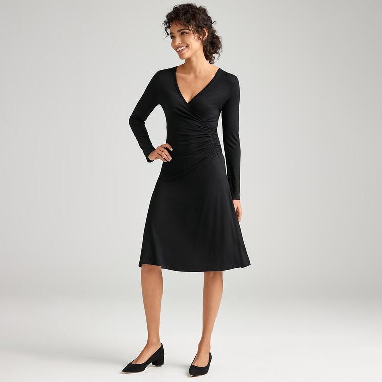 Klaus Dilkrath LBD Frau in schwarzem Kleid mit langen Ärmeln, modisch in einem hellen Raum stehend.