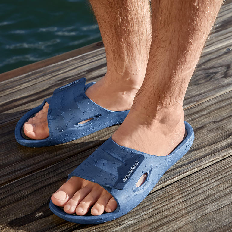 Herren, Blau/Grau Füße in blauen Badeschuhen auf einem Holzdeck am Wasser.