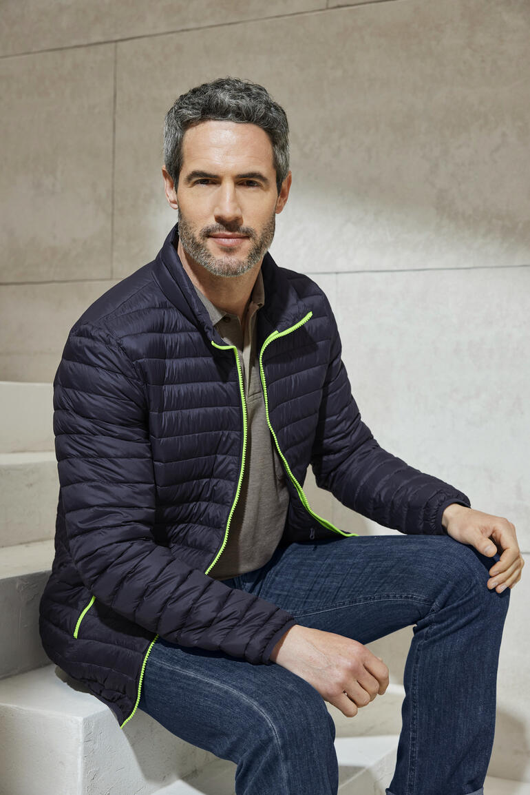 Herren, Navy Mann in schwarzer Sommerdaunen-Steppjacke in einem modernen Raum.