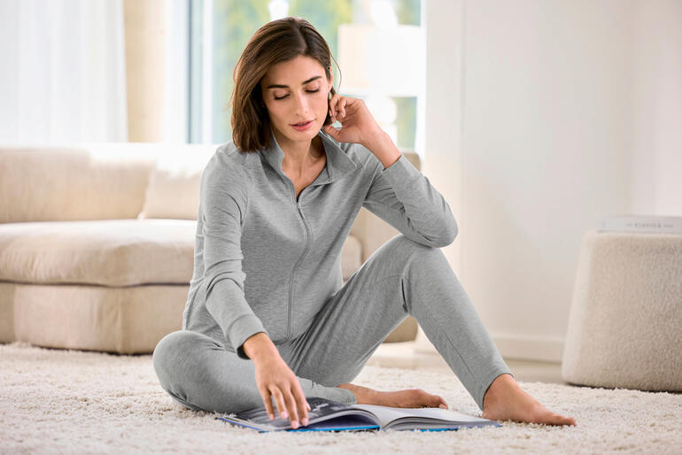 Frau sitzt im grauen Modal-Hausanzug und liest ein Buch.