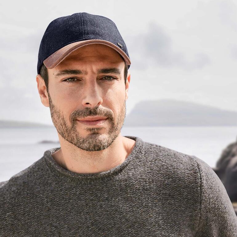 Mann in Fischer-Pullover mit einem dunkelblauen Cap, Blick auf eine Wasserlandschaft.