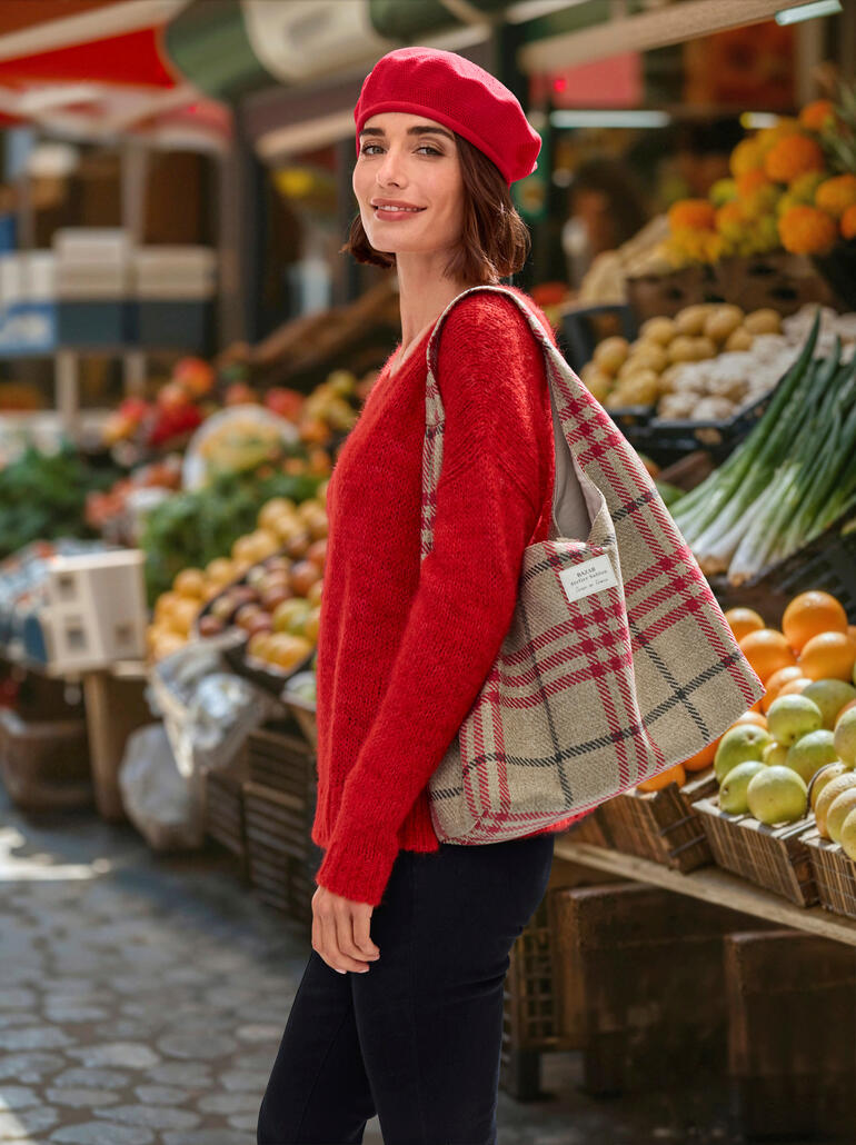Frau trägt rote Baumwoll-Baskenmütze und einen roten Pullover, steht auf einem Markt.