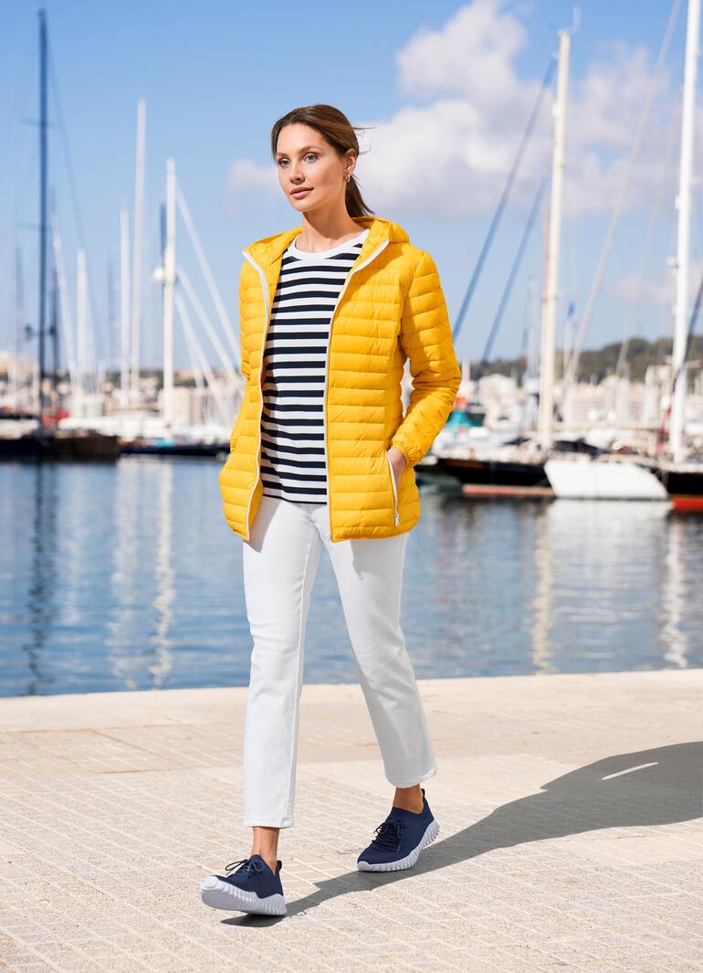 Frau trägt eine gelbe Sommerdaunen-Steppjacke am Hafen