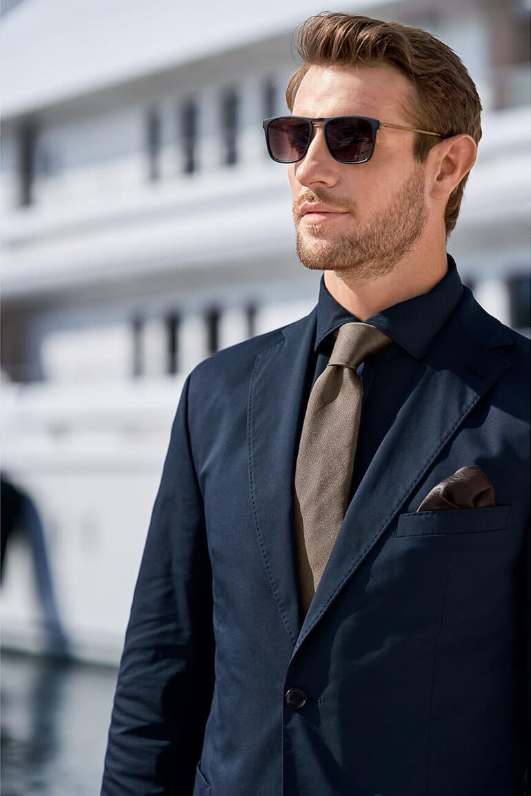 Braun Mann in Anzug mit dunkeloliver Krawatte und Sonnenbrille.