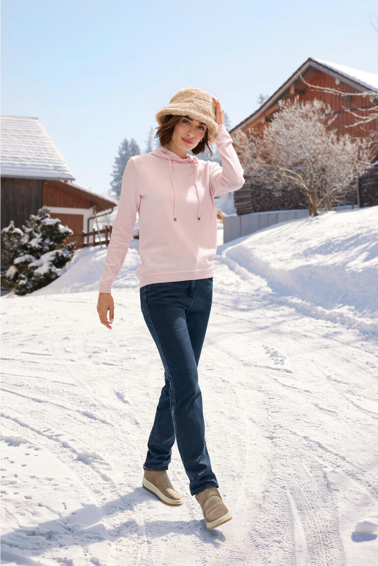 Teddy-Bucket-Hat Frau im roséfarbenen Hoodie beim Spazieren im Schnee.
