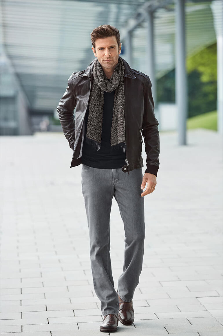 Mann trägt graue T400 Jeans mit schwarzer Lederjacke und Schal