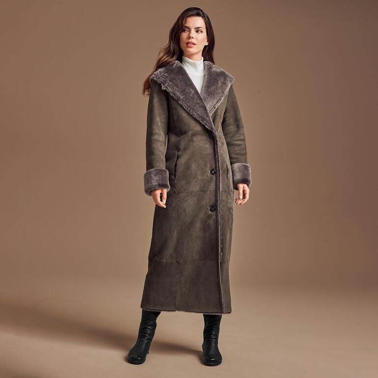 Dame in grauem Lammfell-Wendemantel mit großem Kragen steht auf einem beigen Hintergrund.