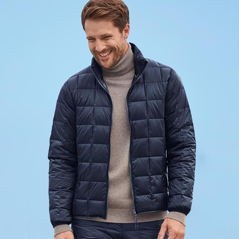 Daunenjacke, Herren und Daunenhose, Unisex Lächelnder Mann in navy Daunenjacke vor blauem Hintergrund.