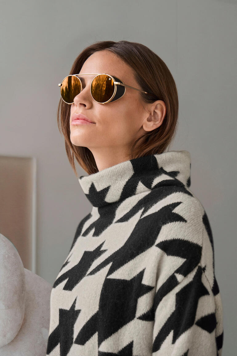 Bogner Gletscher-Sonnenbrille Frau mit Sonnenbrille in gold, trägt einen Pullover mit Sternen-Muster.