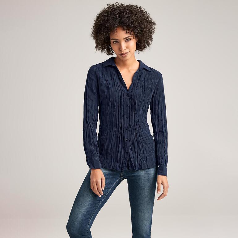 Frau in dunkelblauer bügelfreier Seidenbluse, posierend vor neutralem Hintergrund.