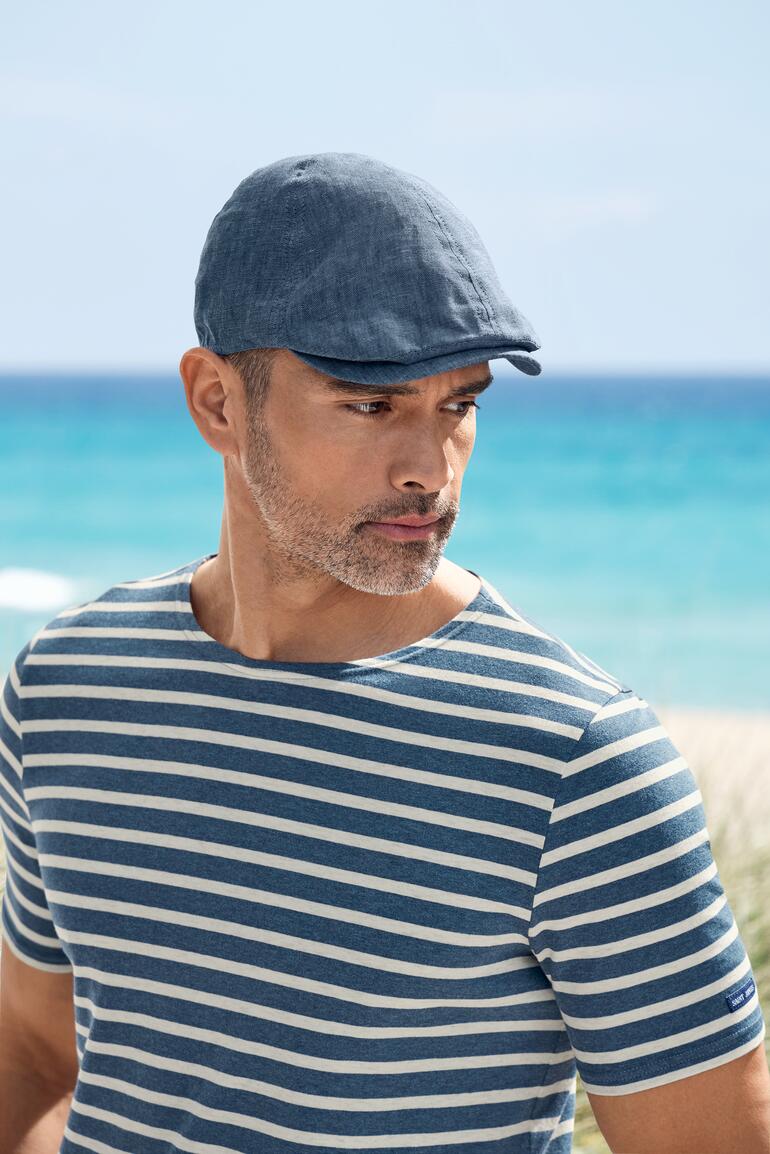 Blau Hochformataufnahme von einem Mann mit Leinen-Schiebermütze am Strand