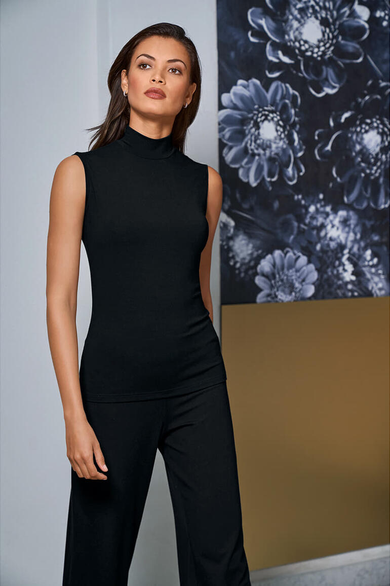 Frau in schwarzem Stehkragen-Top steht vor einer Grafik mit Blumen.