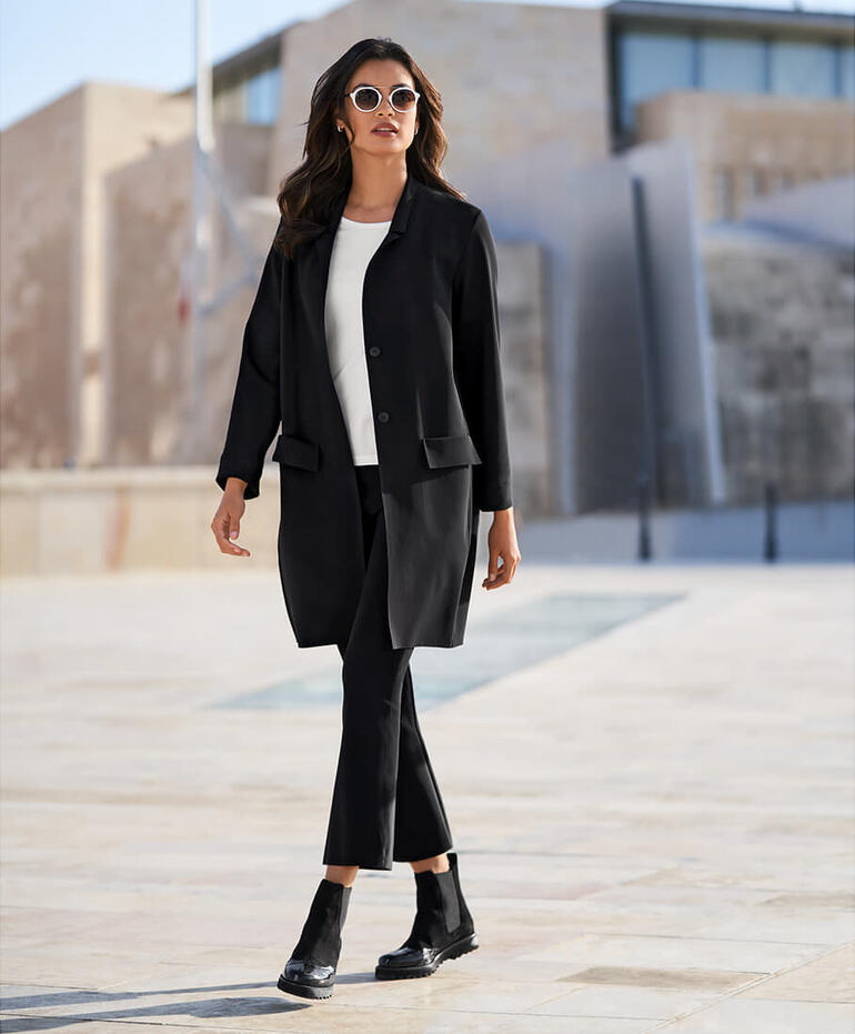 sassenbach Blazer-Mantel Frau trägt einen schwarzen Blazer-Mantel in urbaner Umgebung.