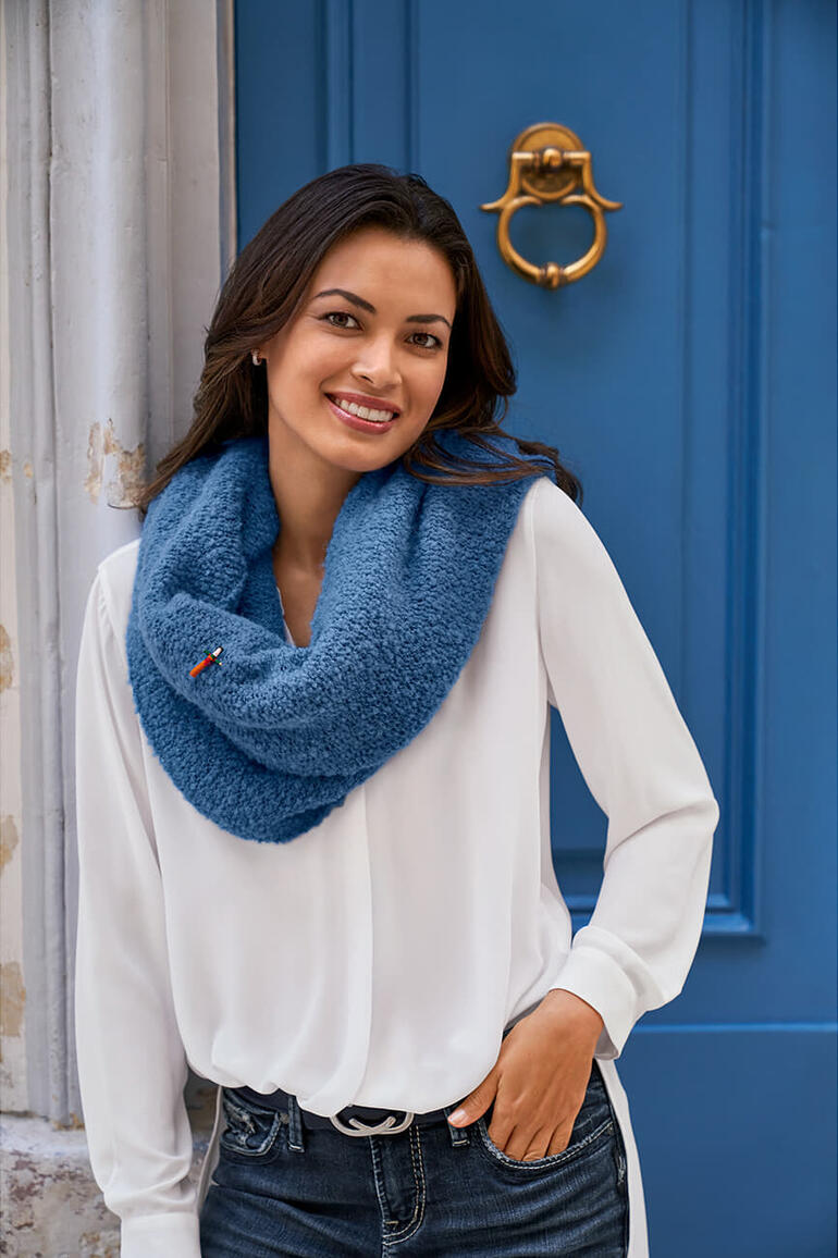 Weiß Frau trägt weißen Bluse mit blauem Bouclé-Poncho vor einer blauen Wand