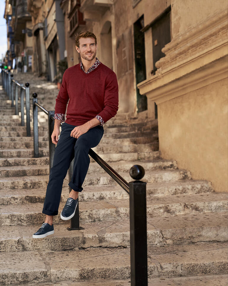 Rot Mann in rot meliertem Leinenpullover sitzt auf Steintreppen in einer Stadt.