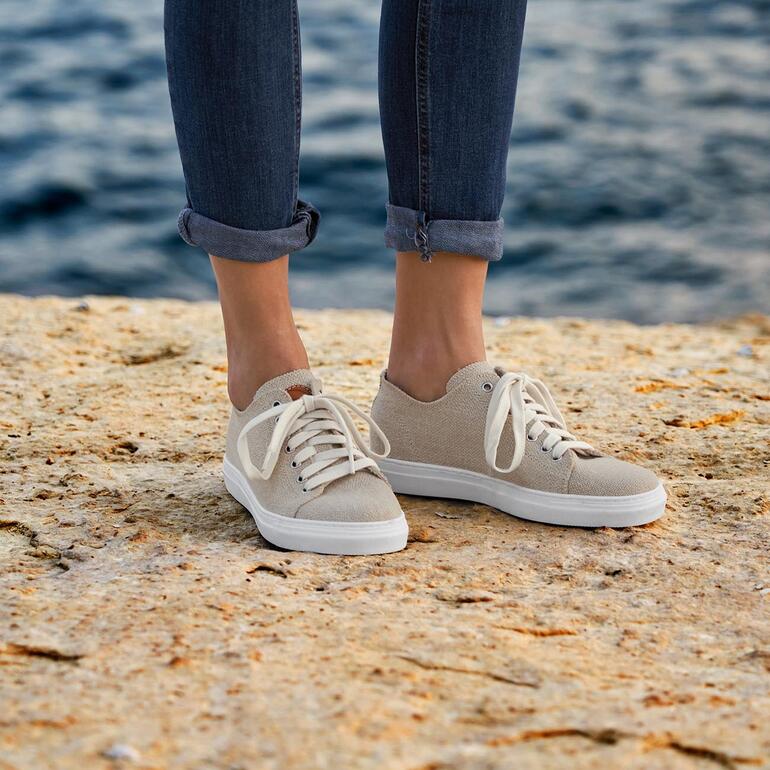 Damen Beige Risorse Future Hanf-Sneaker an Füßen an einer Küstenlinie