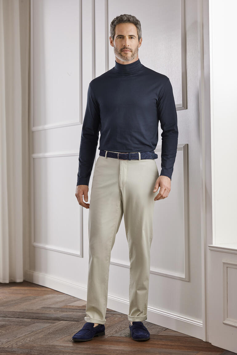 Sunspel Unterzieh-Rolli Mann im dunklen Sunspel Unterzieh-Rolli und heller Hose in einem eleganten Raum.