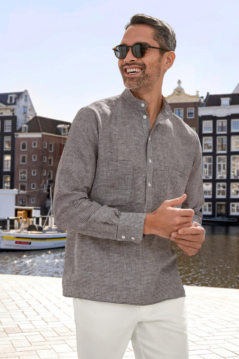 Lächelnder Mann in kariertem Nehru-Leinenhemd vor Wasser in der Stadt.