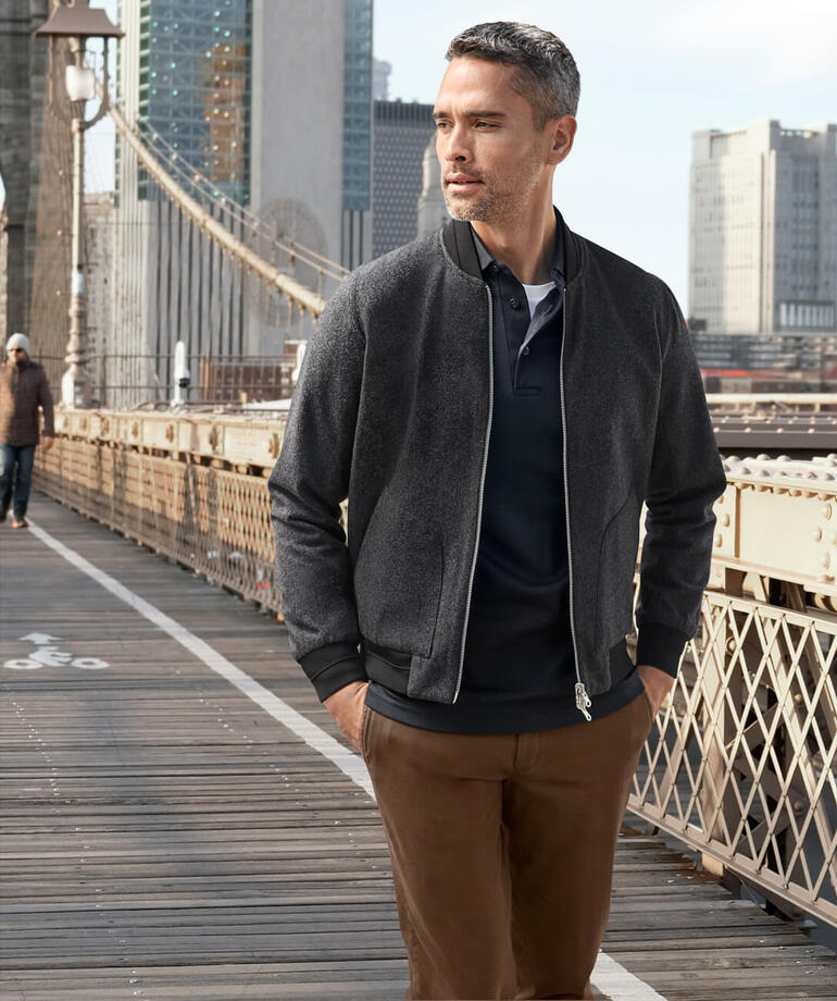 Mann trägt einen Wende-Blouson, Gehweg mit Stadtansicht im Hintergrund.