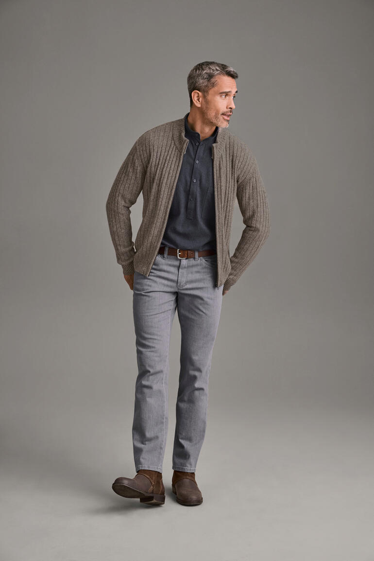 Yak-Strickjacke Mann in einem beigen Yak-Strickjacke über einem blauen Hemd und grauen Hosen
