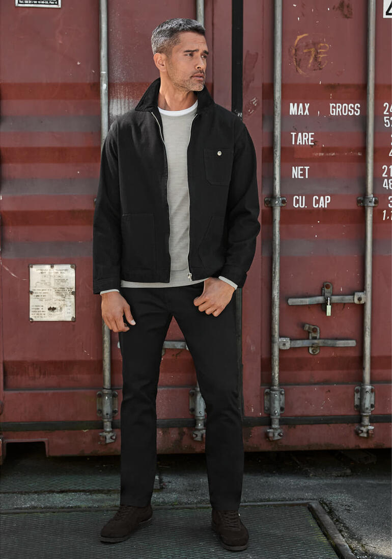 Mann in schwarzer Edwin Selvage-Jeansjacke steht vor einem Container.