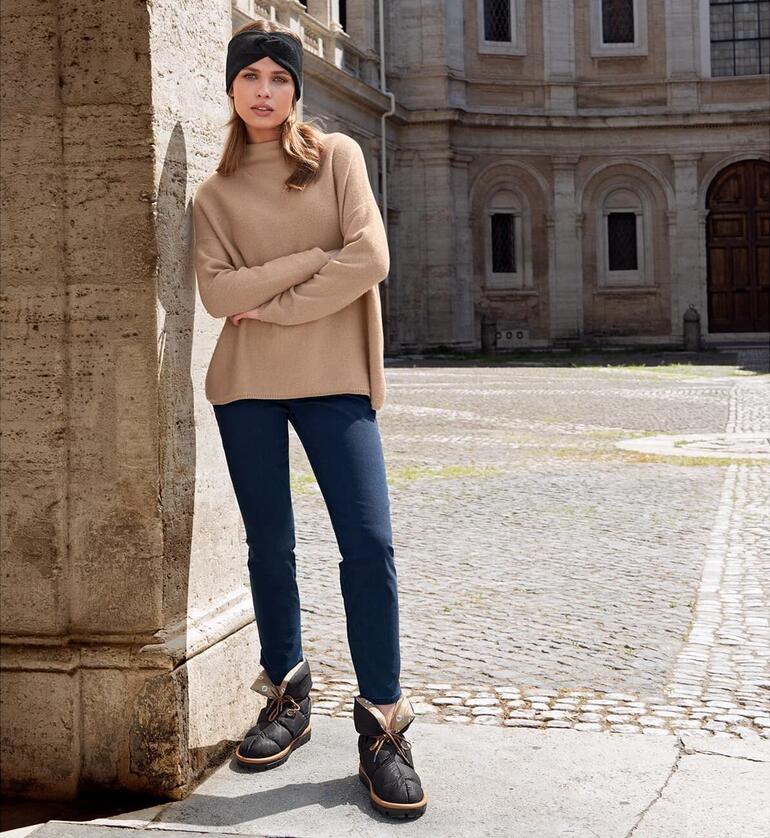 Schwarz Frau in beigem Pullover und Blauen Jeans steht mit Flufié Daunen-Sockboots auf Steinboden.