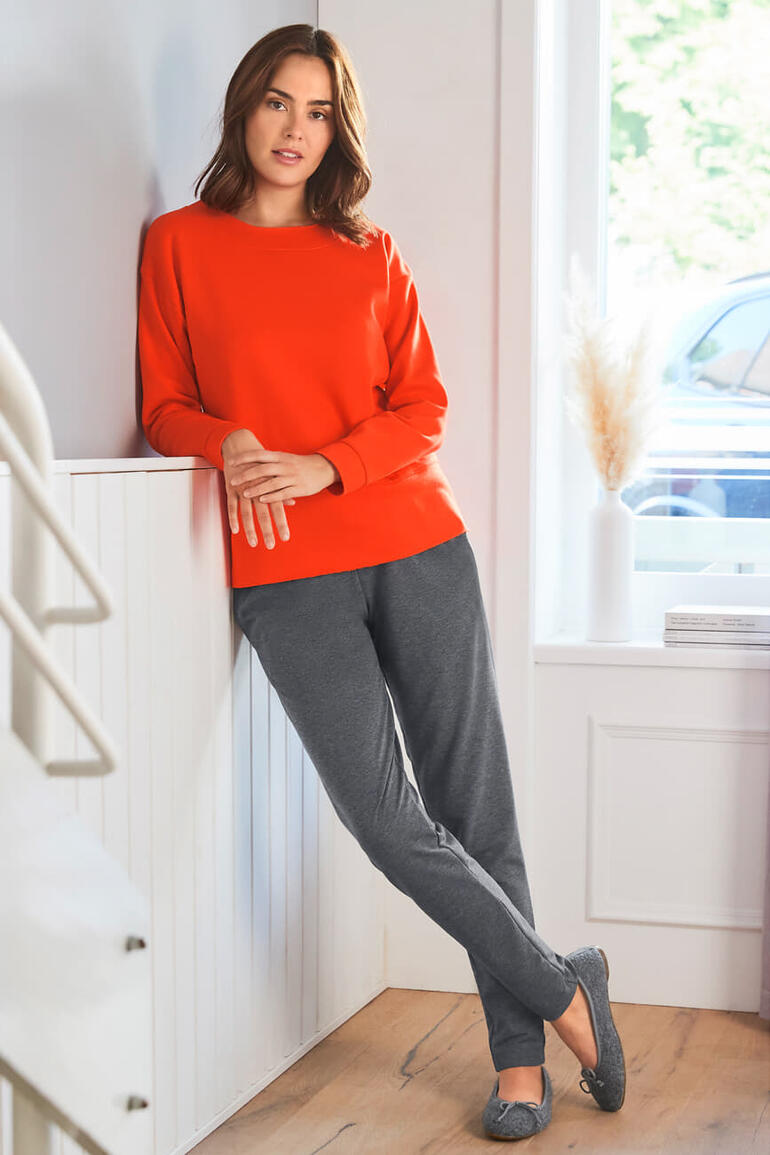 Gottstein Walk-Ballerina Frau in rotem Sweatshirt und grauen Jogginghosen lehnt an einer Treppe.