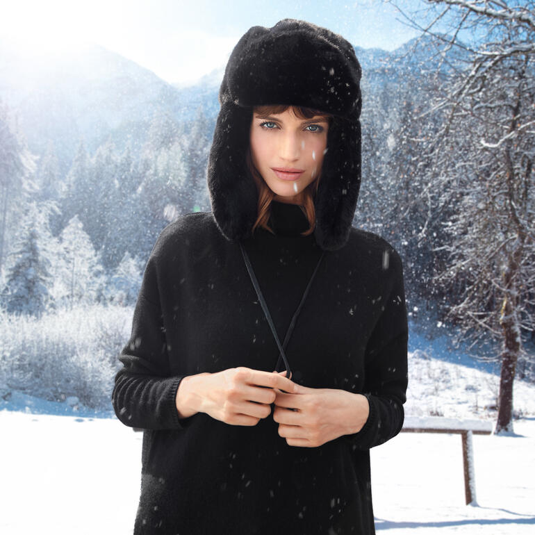 Frau trägt eine Faux-Fur-Schapka in einem verschneiten Landschaftsbild.
