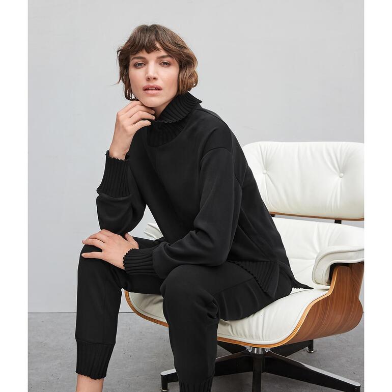 Frau in schwarzem Sweater sitzt entspannt auf einem weißen Sessel.