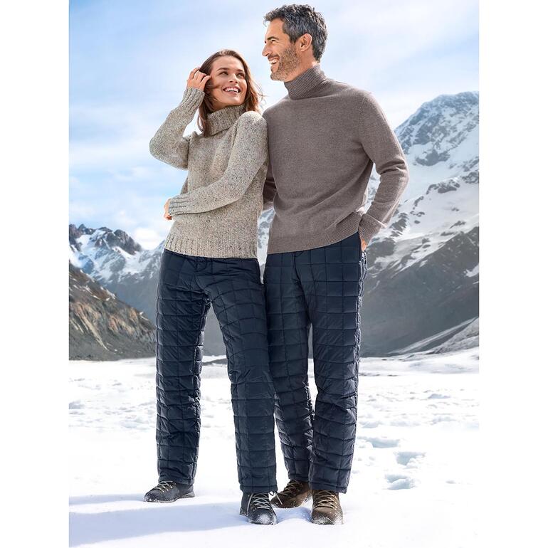 Paar Modelle stehen in Daunenjacke und -hose in bergiger Landschaft