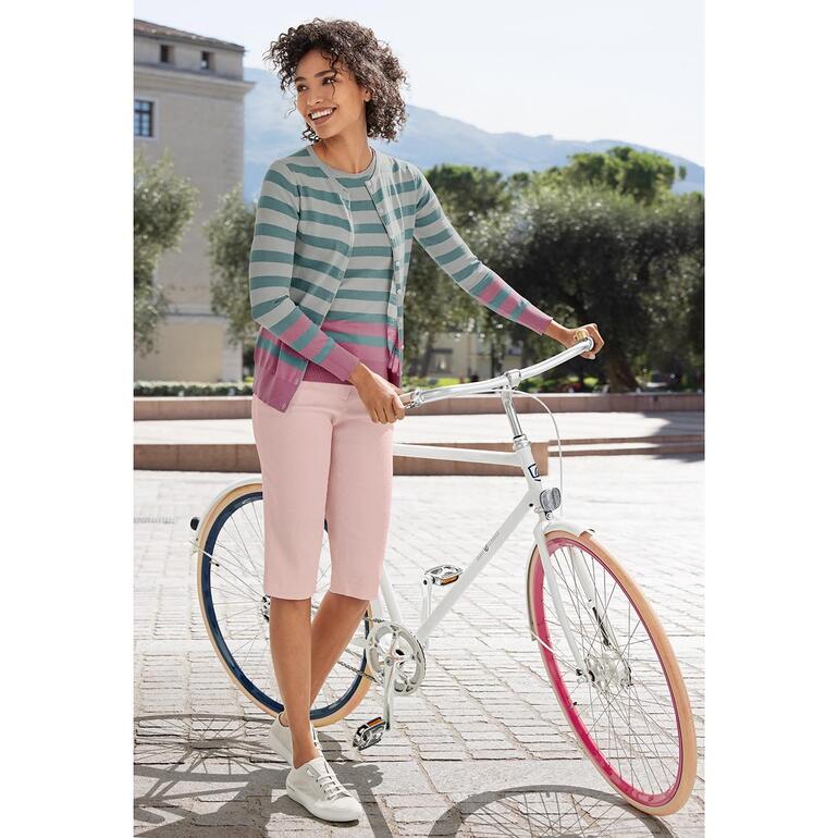 Petrol/Ecru/Pink Frau in einem gestreiften Oberteil und rosa Hose steht neben einem Fahrrad.